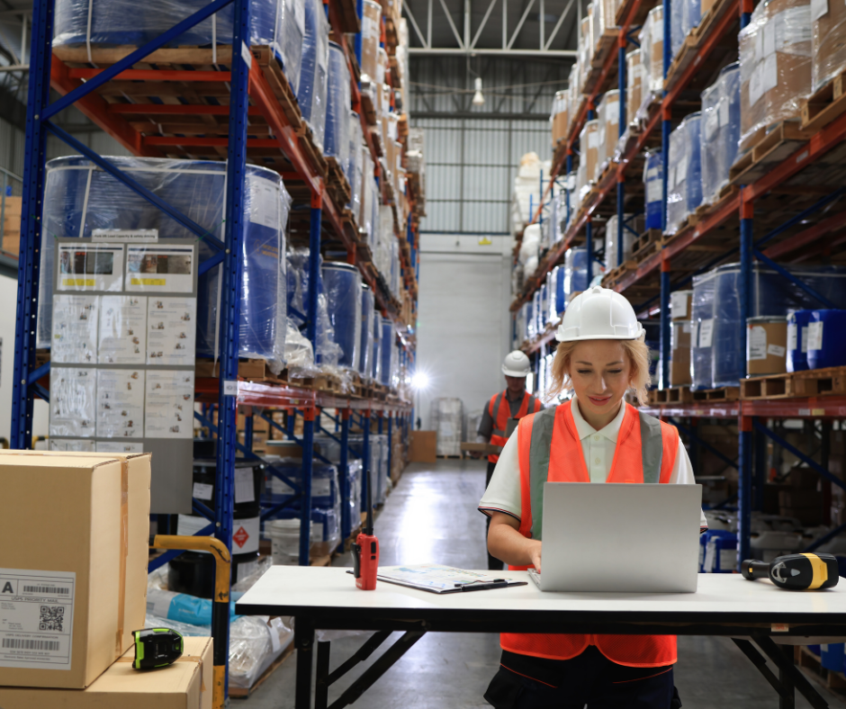 Warehouse Worker on Computer Next to Stocked Shelves | JIT Inventory Management: Pros & Cons | Learn JIT Inventory Managements